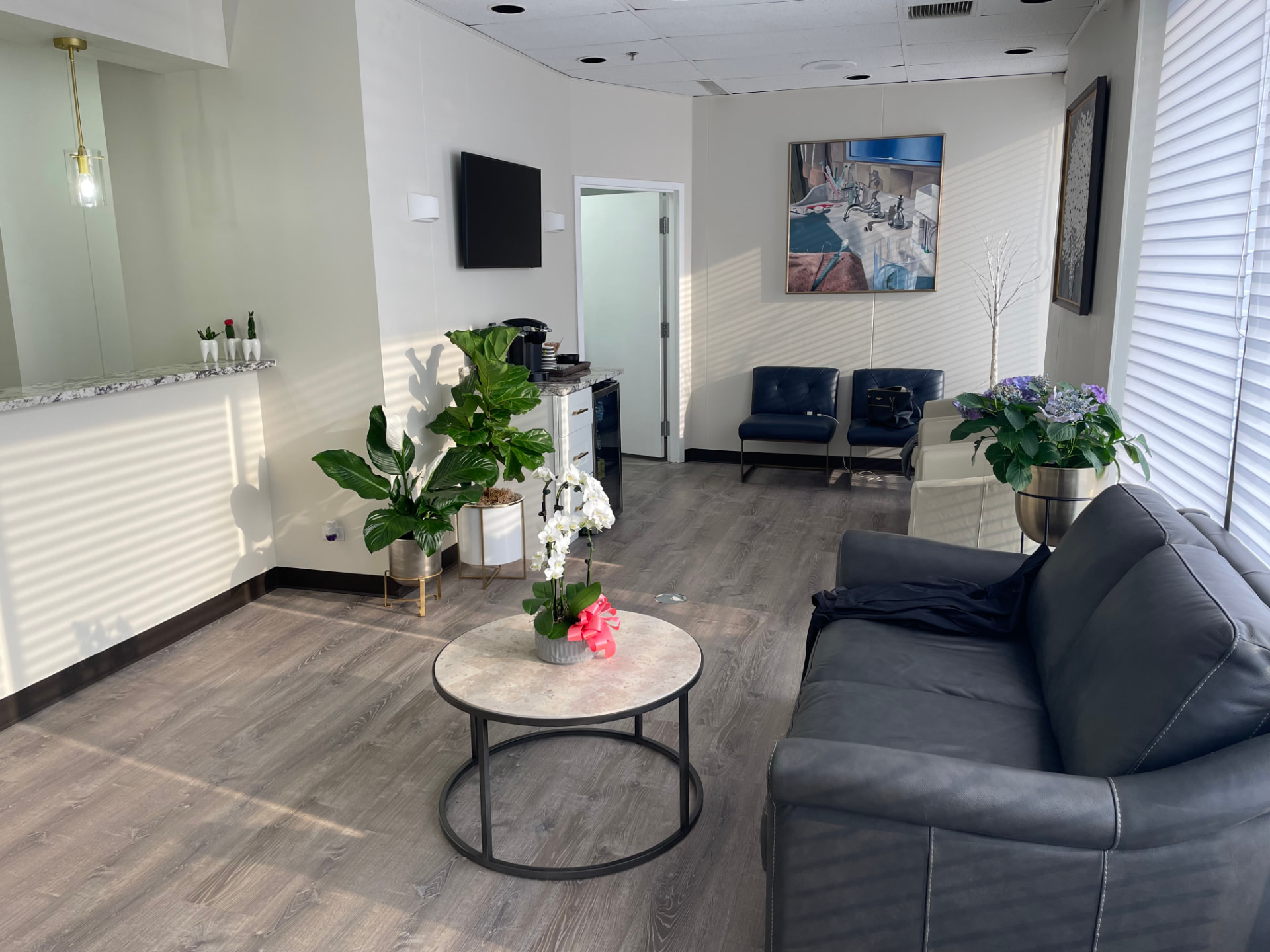 Sunlit waiting room with leather seating, plants, and a coffee station
